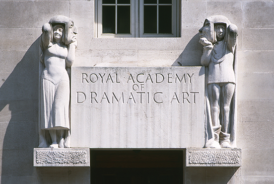 Entrance sculpture to RADA. Two figures with theatrical masks either side of a sign in grey stone. 