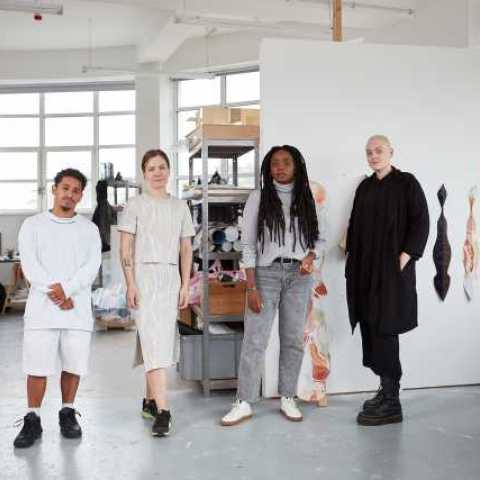 The Image depicts four Acme artists standing next to each other in their studio at Warton House, London. Artists from left to right: Bryan Giuseppi Rodriguez Cambana, Kristīne Daukšte, Lisa-Marie Harris, Holly Buckle.