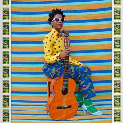 Hassan Hajjaj, My Rockstar Series, Bumi Sittin' - women sits with guitar in brightly coloured clothes against fabric backdrop