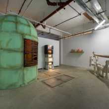 Exhibition image featuring large cylindrical green kiosk, stacked microwave sculpture  