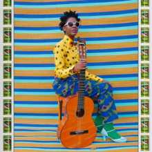 Hassan Hajjaj, My Rockstar Series, Bumi Sittin' - women sits with guitar in brightly coloured clothes against fabric backdrop