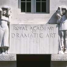 Entrance sculpture to RADA. Two figures with theatrical masks either side of a sign in grey stone. 